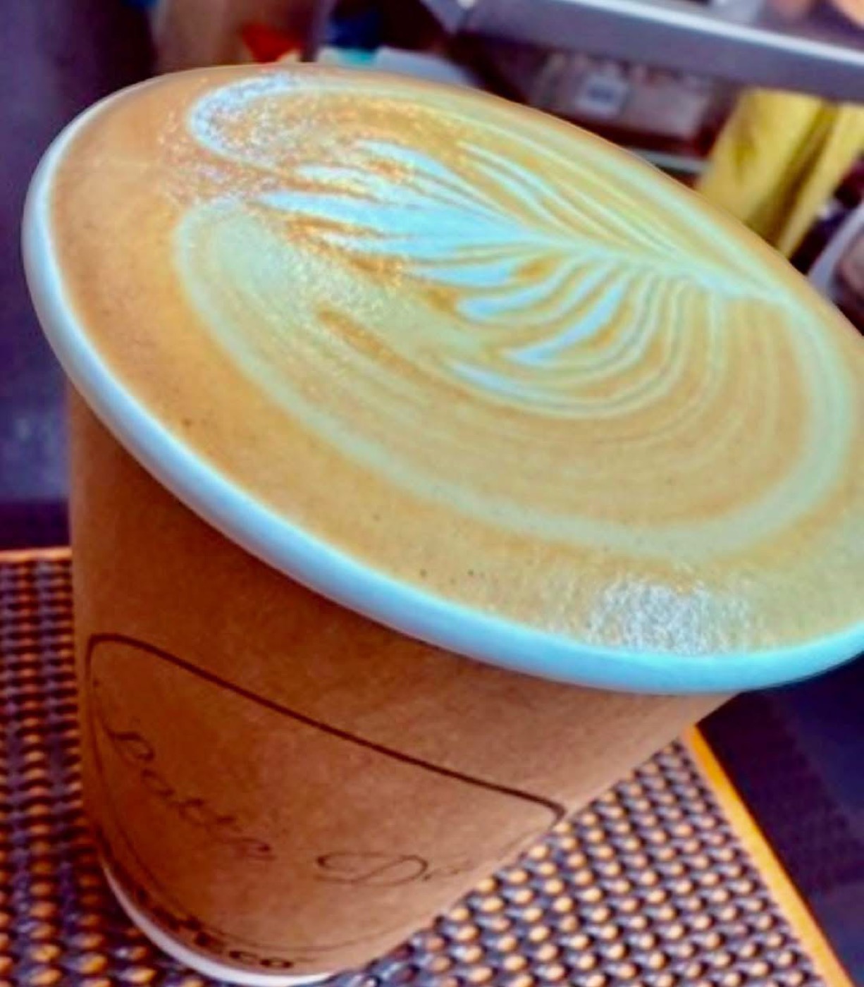 A takeaway latte in a Latte Dah cup with a feather pattern in the milk foam
