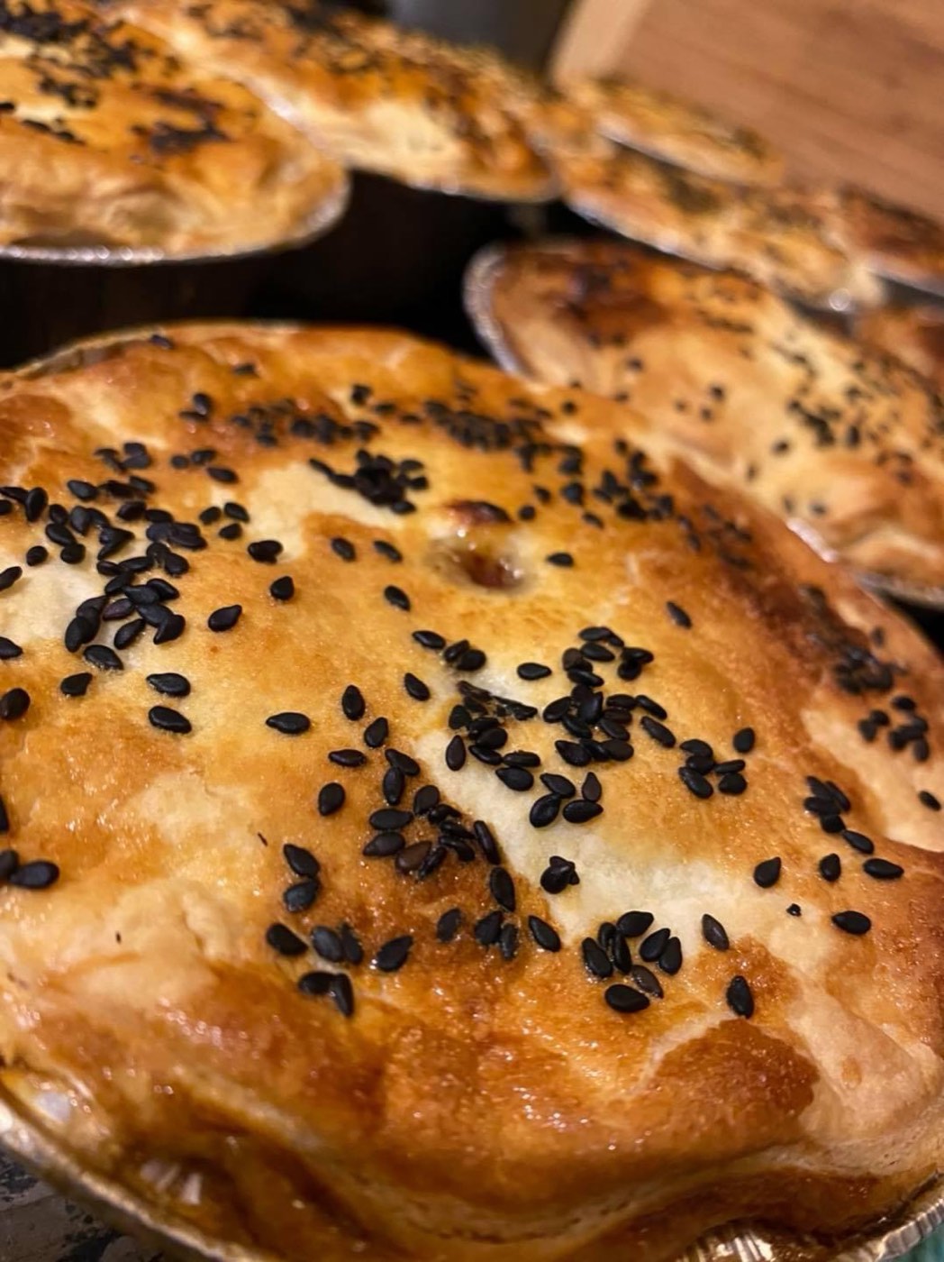 A golden pie topped with black sesame seeds, with more pies behind it